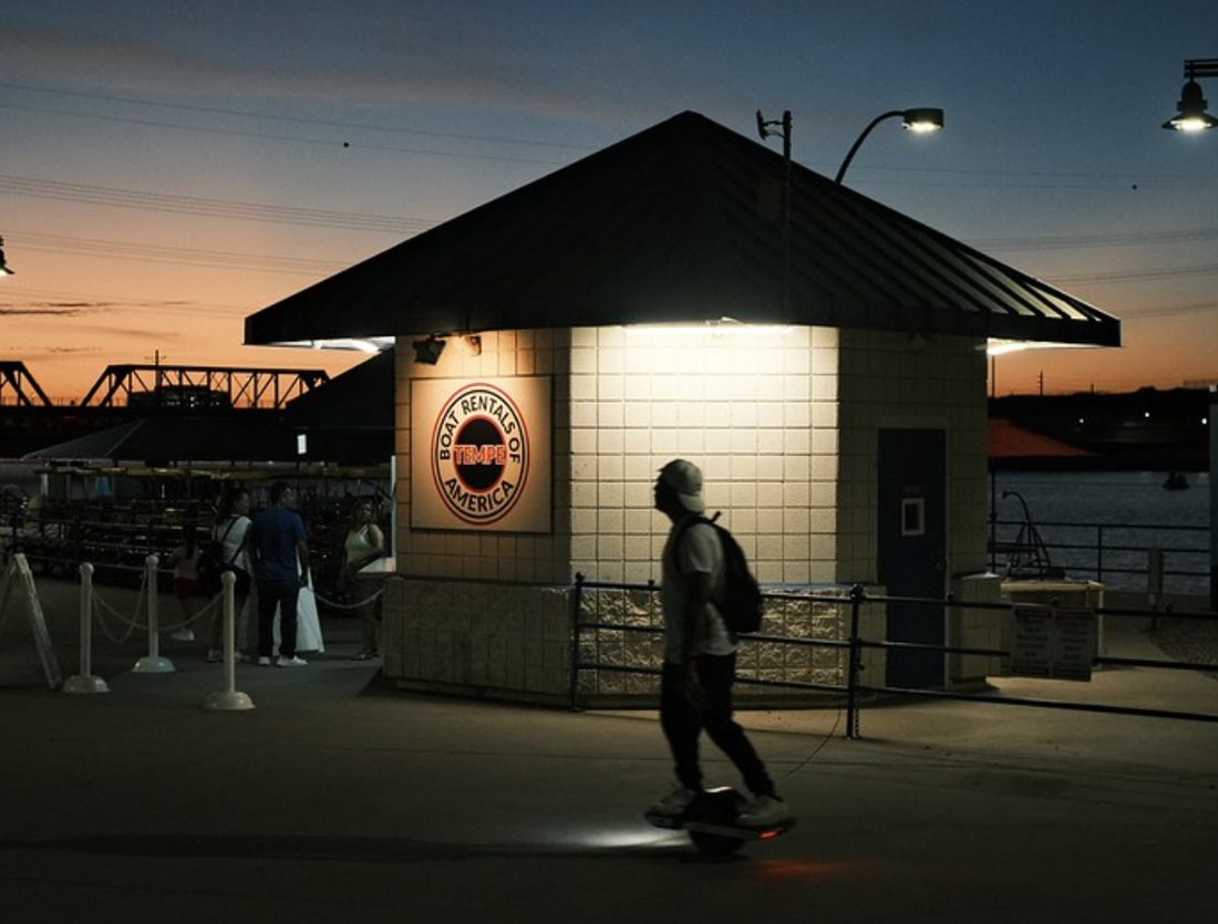 pellicule couleur froide — une scène urbaine au crépuscule, un skateur passant devant un kiosque éclairé sur les quais